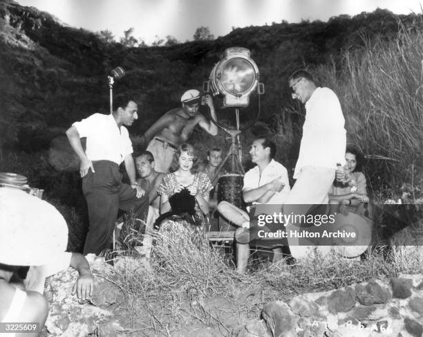 Swedish-born actor Ingrid Bergman knits while sitting with Italian director Roberto Rossellini and a film crew outdoors on the set of Rossellini's...