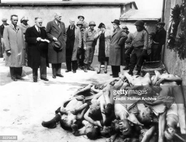 Full-length view of British MPs, a journalist, and soldiers standing behind a heap of emaciated naked corpses at the concentration camp in...