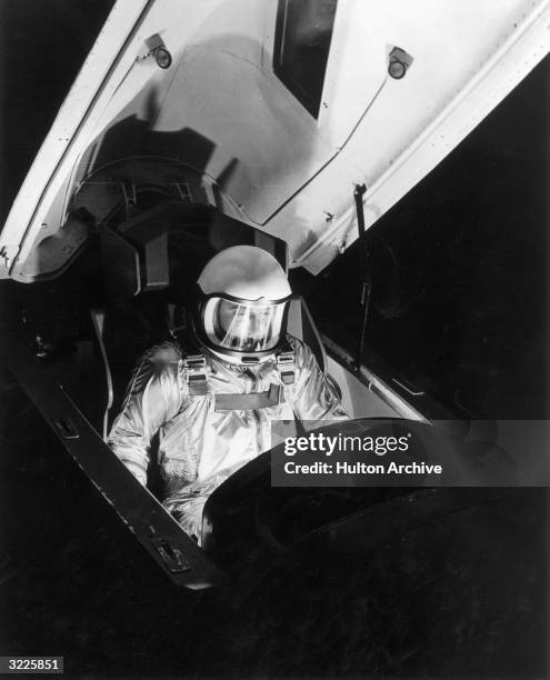 Military pilot sits in the cockpit of an X-15 experimental rocket aircraft, wearing an astronaut's spacesuit.
