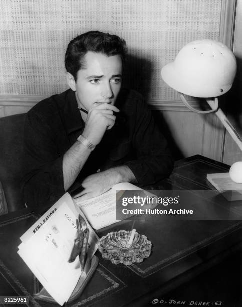American actor John Derek sits at a desk and studies a script for his role in director Fred F. Sears's film, 'Mission over Korea'. Also on the desk...