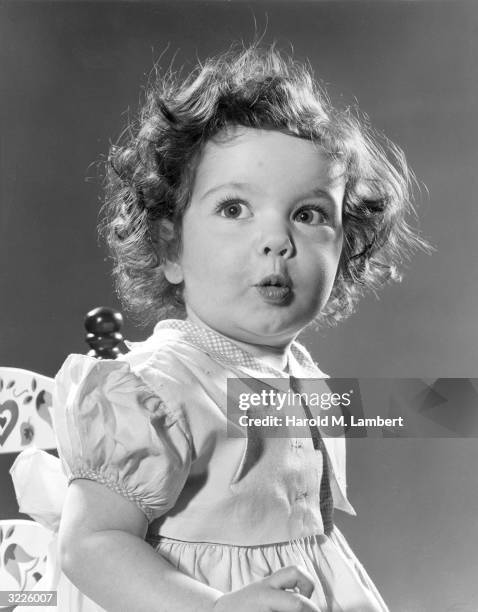 Little girl with brown curly hair sits in a chair making a face.