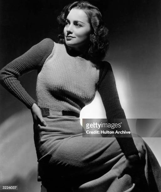Studio portrait of British-born actor Olivia de Havilland sitting on a stool and looking over her shoulder as she rests her hand on her hip. De...