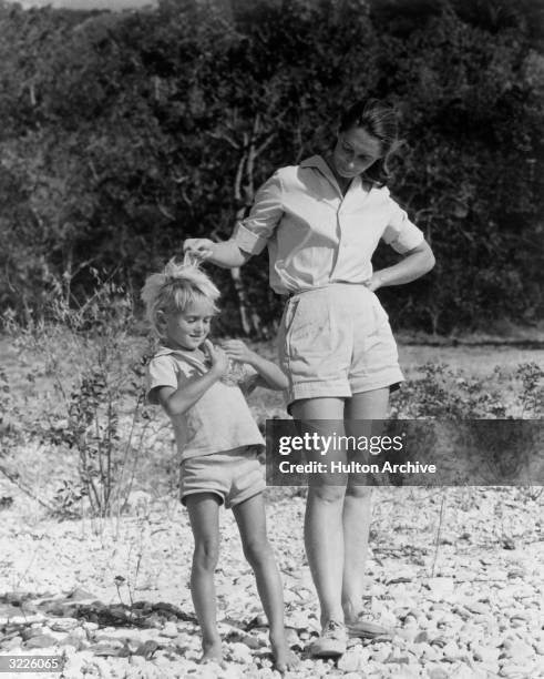 Full-length portrait of British anthropologist and expert on chimpanzees Jane Goodall standing outdoors in shorts and running her fingers through the...