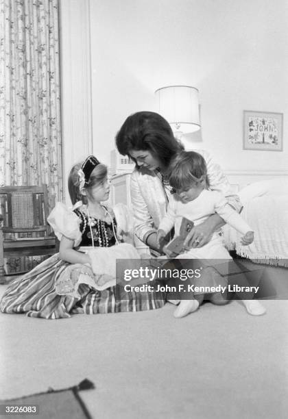 American First Lady Jacqueline Bouvier Kennedy kneels on the bedroom floor, reading a storybook to her children, John F. Kennedy Jr. And Caroline...