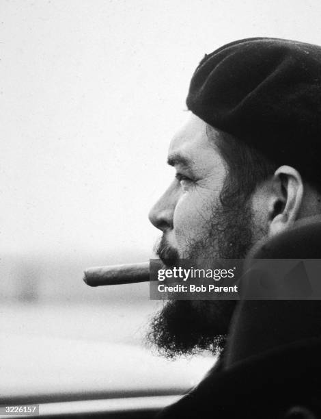 Profile portrait of Argentine-born Cuban Marxist revolutionary Ernesto 'Che' Guevara wearing a beret and smoking a cigar in an airport, probably New...