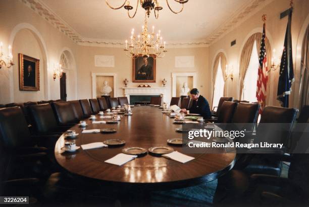 President Ronald Reagan sits alone at a long polished oak table in the cabinet room, looking through documents, at the White House, Washington, DC. A...