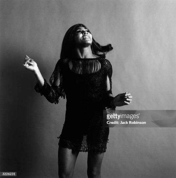 Studio portrait of American rock singer Tina Turner, wearing a dark crocheted mini-dress, looking up and snapping her fingers while singing, New York...