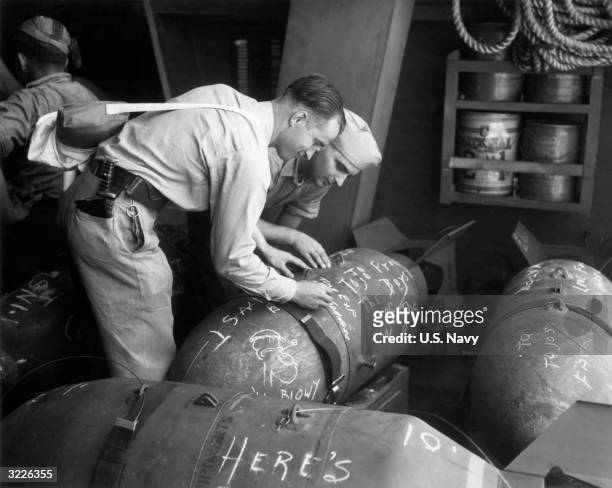 Navy servicemen E S Cornwell of California and T J Carpenter of Michigan use chalk to write greetings to Japanese minister of war and premier Hideki...