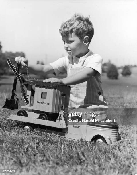 Young boy kneels in a field, playing with his toy flatbed truck and bulldozer.