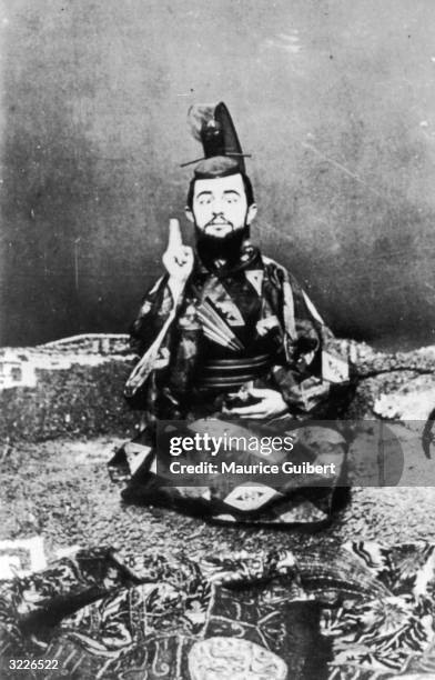Portrait of French painter and graphic artist Henri Toulouse-Lautrec posing as a Japanese emperor while sitting cross-legged and cross-eyed on an...