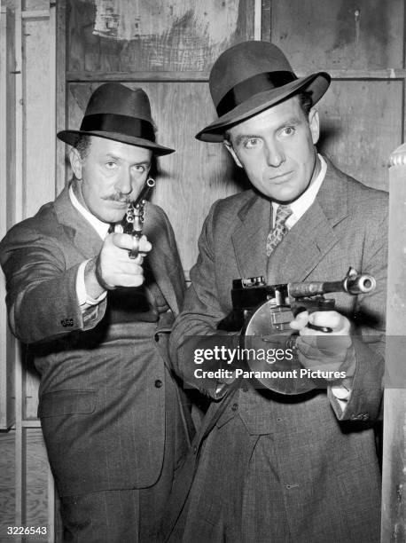 American actor Robert Stack playing Eliot Ness, and American actor Keenan Wynn , playing Ness' cohort Joe Fuselli, aim their guns while raiding an Al...