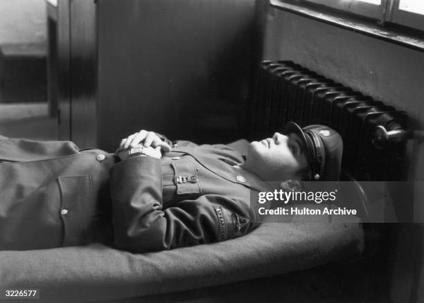 Portrait of American rock singer Elvis Presley , wearing a military uniform, lying on an army cot with his hands folded across his chest.