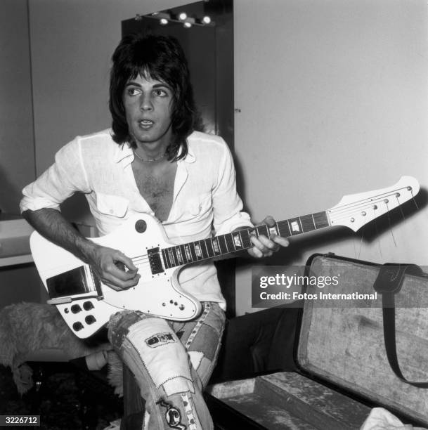 Australian-born actor and pop singer Rick Springfield sits on the arm of a couch, playing his electric guitar backstage before a concert at Knotts...