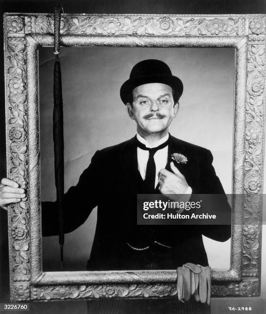 Scottish actor David Tomlinson smiles while posing behind a gilt picture frame in a promotional portrait for director Robert Stevenson's film, 'Mary...