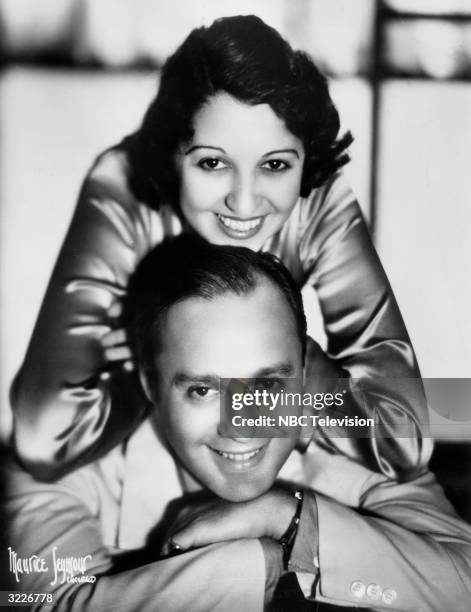 Promotional headshot portrait of American comedian Jack Benny and his wife, Mary Livingstone, leaning on his shoulders, both smiling, taken for a...