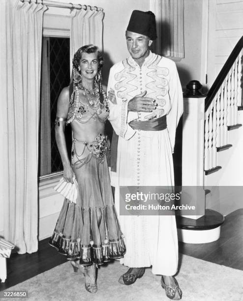 Full-length image of American actor Gary Cooper posing with his wife, Sandra Shaw 'Rocky' , wearing Middle Eastern costumes. Cooper wears a fez, a...