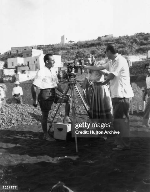 Swedish actor Ingrid Bergman smiles behind a motion picture camera as her husband, Italian film director Roberto Rossellini points to the lens,...