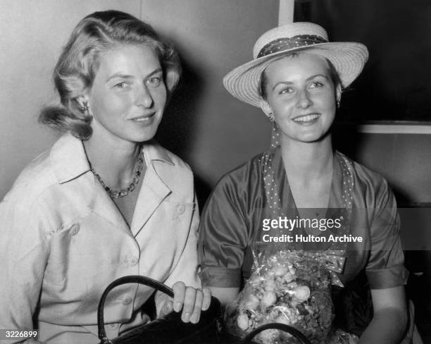 Swedish-born actor Ingrid Bergman smiling and sitting with her daughter Pia Lindstrom. Lindstrom is holding a bouquet of flowers in her hand and is...