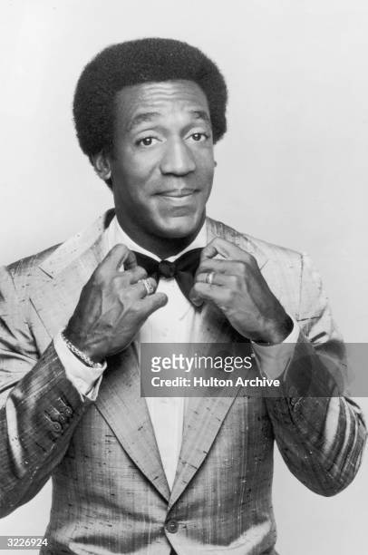 Promotional studio portrait of American actor and comedian Bill Cosby adjusting his bow tie, from his television series, 'The Bill Cosby Show'.