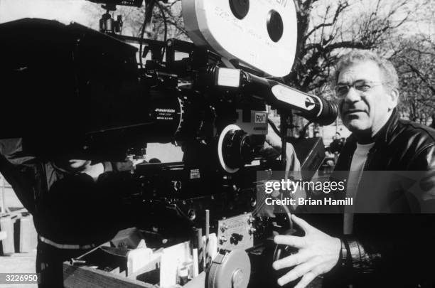 American director Sydney Pollack stands outside, looking into a movie camera on the set of his film, 'Sabrina'.