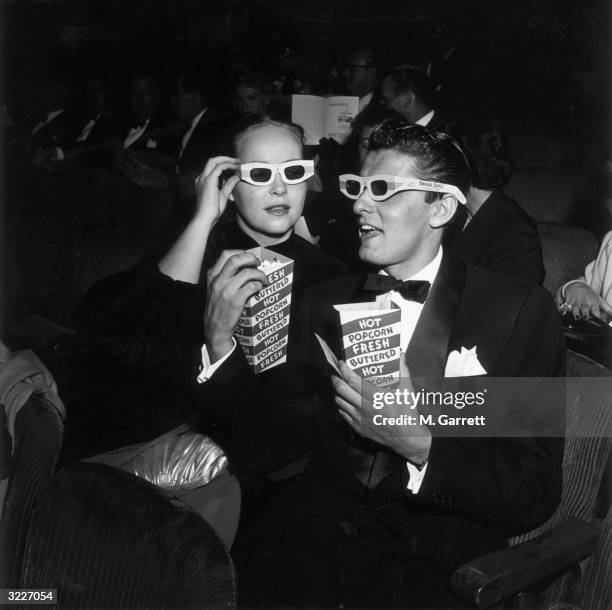 American actor Keefe Brasselle and his wife Norma, wearing 3-D glasses and holding boxes of hot buttered popcorn, sit in the theater at the premiere...