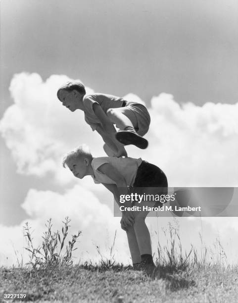 One boy jumps over the back of another boy, playing a game of leap frog outdoors.