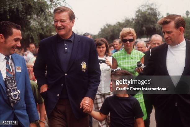 American actor John Wayne holding the hand of his young son, John Ethan, while on a visit to the Knott's Berry Farm amusement park, Buena Park,...