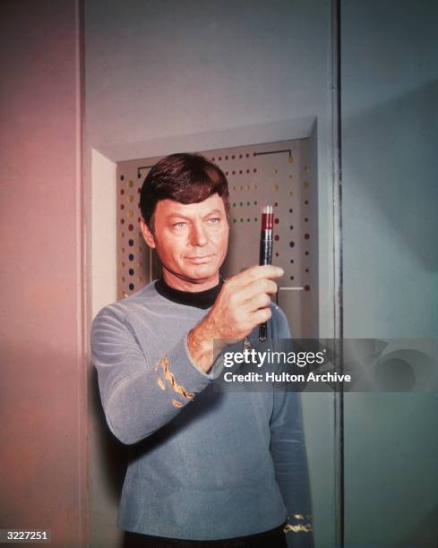 American actor DeForest Kelley , portraying Dr 'Bones' McCoy, examines a vial filled with a dark substance in a still from the television show, 'Star...