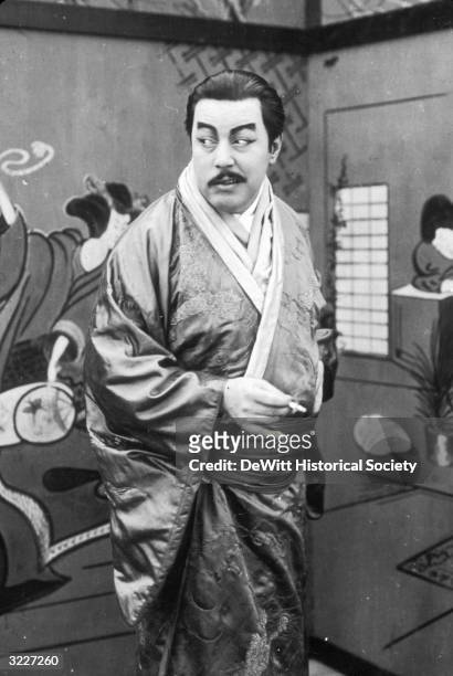 Swedish actor Warner Oland, made up to look Asian, wearing a kimono and smoking in a still from the silent film 'Patria'.