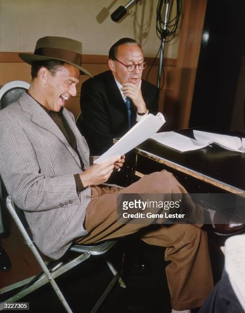 American singer and actor Frank Sinatra sits and laughs, as he reads a screenplay with American comedian Jack Benny in a radio studio. Sinatra is...