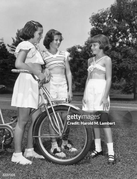 Three young girls standing with a bicycle outdoors on the grass.