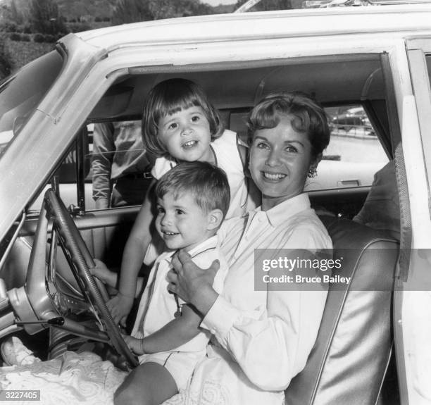 American actor Debbie Reynolds smiles while sitting in the front seat of an automobile with her children Todd and Carrie Fisher, Hollywood,...