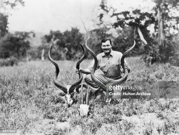 American writer Ernest Hemingway kneels while holding a pair of antelope horns during a safari, Africa.