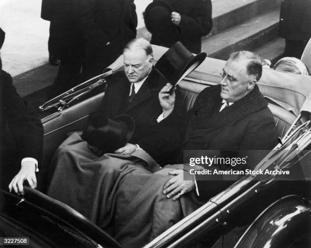 President Roosevelt tips his top hat while sitting in the back of a car with former President Herbert Hoover at the inauguration in Washington D.C.