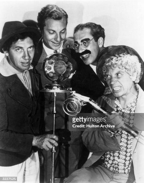 Promotional portrait of the Marx Brothers clowning around a microphone. Harpo is holding a fumigator.