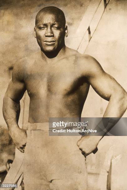 Portrait of boxer Jack Johnson , the first African-American to win the heavyweight crown, standing barechested with his hands on his hips.