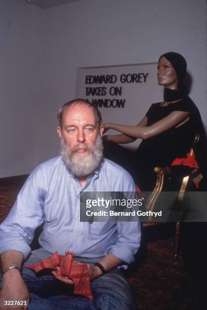 American illustrator and author Edward Gorey sits in front of a female mannequin, holding a stuffed toy bat. A sign behind him reads, 'Edward Gorey...