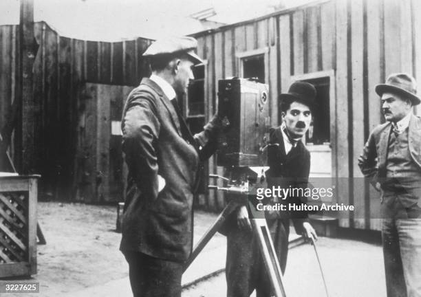 British actor and director Charles Chaplin , in costume as the Tramp, looks into a movie camera as two cameramen stand by in a still from director...