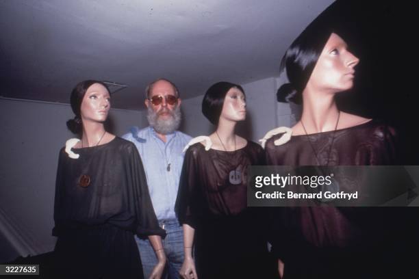 American illustrator and author Edward Gorey poses with three female fashion mannequins clothed in sheer black gowns with metal pendants. Gorey was...