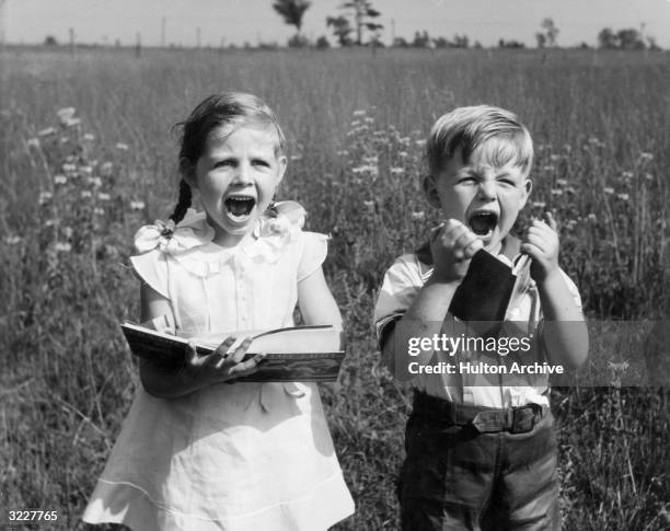 Young boy and girl stand in a farm field holding storybooks and screaming.