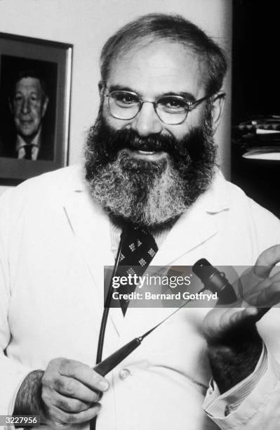 Portrait of British-born neurologist Dr Oliver Sacks smiling while holding a mallet in a white lab coat.