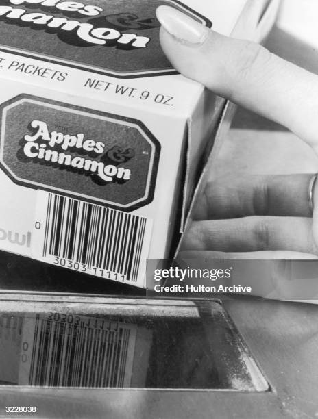 Closeup of a boxed food item with a numerical UPC code being dragged across an optical scanner window for the supermarket checkout line.