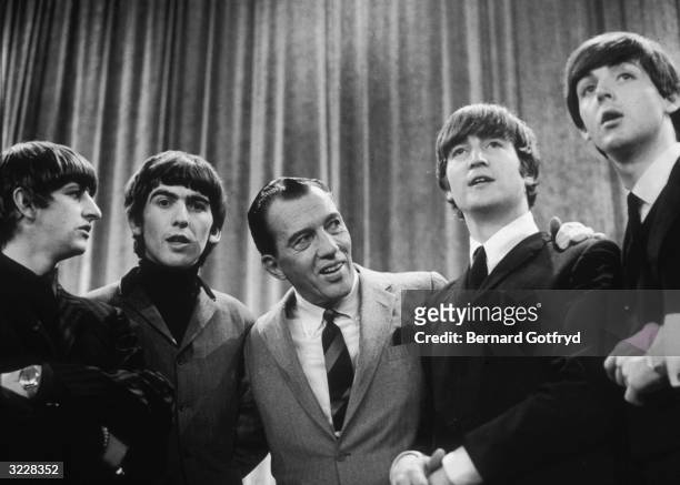American television host Ed Sullivan smiles as he stands, with the members of British rock group the Beatles, on the set of his television variety...