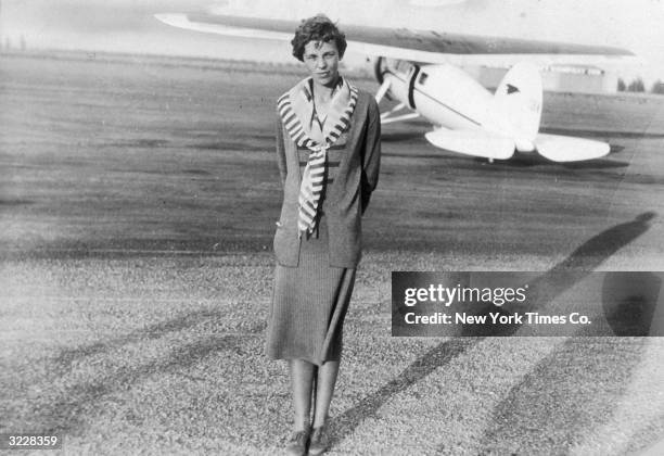 Full-length image of American aviator Amelia Earhart standing on an airstrip in front of her White Lockeed Vega Monoplane, in which she broke a speed...