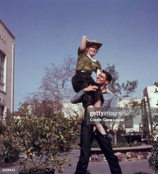 American actor Marilyn Monroe sitting on American actor Don Murray's shoulder while clowning on the set of director Joshua Logan's film 'Bus Stop'.