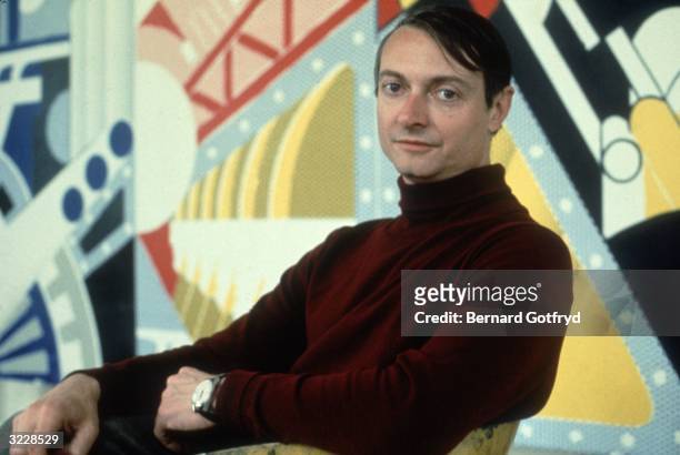 Portrait of American artist Roy Lichtenstein seated before one of his works.