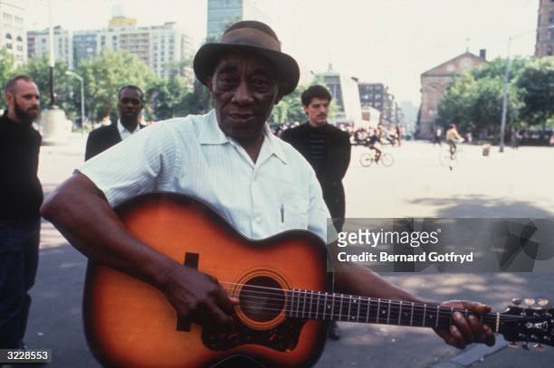 American blues musician Mississippi John Hurt plays a guitar while standing in Washington Square Park, New York City.