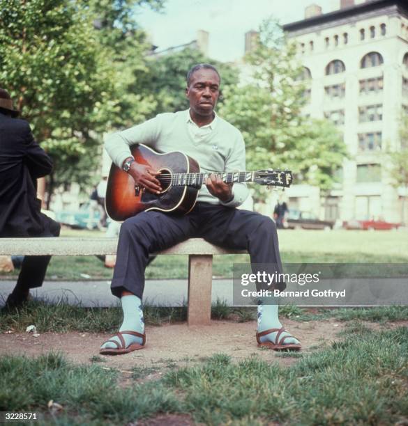 American blues musician Skip James plays guitar while sitting on a bench in Washington Square Park, New York City. Musician Mississippi John Hurt...