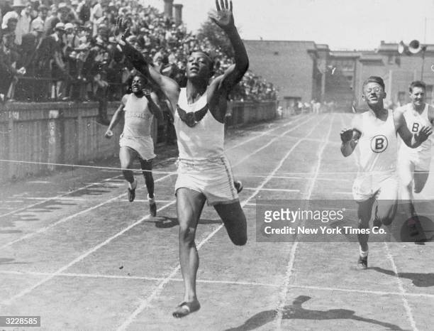 Cleveland high school student and future Olympic champion Jesse Owens holds his hands in the air while crossing a finish line to break the world...