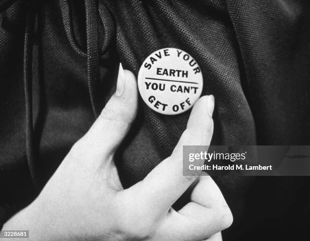 Close-up of a hand holding up an Earth day button which reads, 'Save your Earth - You can't get off.'